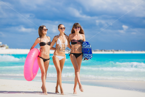 Three slim young girls in bikinis on the beach. Group of Three Beautiful Attractive Young Women Walking on the Beach. happy girl friends having fun at the beach while on vacation