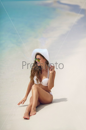 Happy woman enjoying beach relaxing joyful in summer by tropical blue water. Beautiful white bikini model happy on travel wearing beach sun white hat on ocean beach, Big Island, Hawaii, USA.