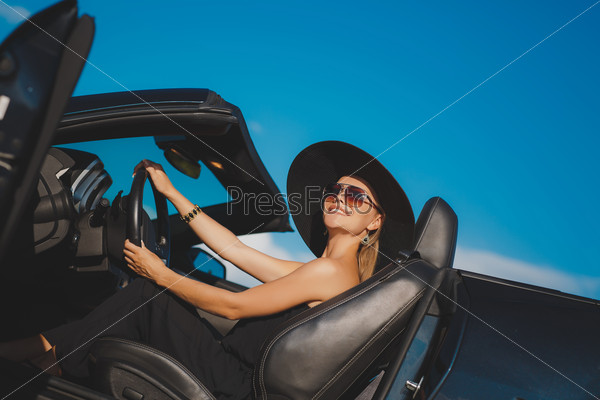 Smiling woman sitting in car, Happy girl driving automobile, outdoors summer portrait.  Young woman driving on road trip on beautiful sunny summer day.Portrait sexy fashion woman model in sunglasses