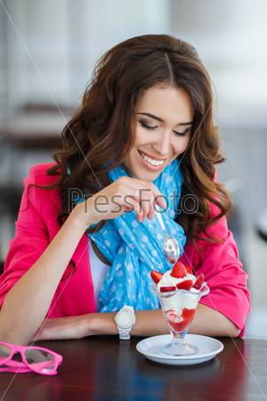 Beautiful young woman happy smiling & looking at camera sitting in restaurant or cafe and eating ice cream closeup portrait, smiling and looking in camera. young beautiful woman eating a dessert