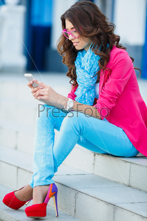Young Woman with smartphone walking on street, downtown. Young girl sitting on the stairs using cell phone. Emotional smiling portrait.