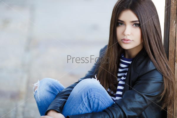 young woman outdoor. portrait of young beautiful woman in a black leather jacket. beautiful girl portrait. Beautiful fashionable woman sitting on the ground