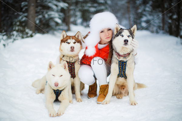 Happy young woman playing with siberian husky dogs in winter forest. Beautiful girl hugging the dog. The girl with the siberian husky