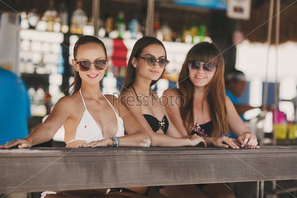 three beautiful sexy women in bikini in bar on Hawaii at beach bar. Beautiful girls enjoying alcoholic beverage cocktail outside. Smiling happy Caucasian women on Hawaiian beach.