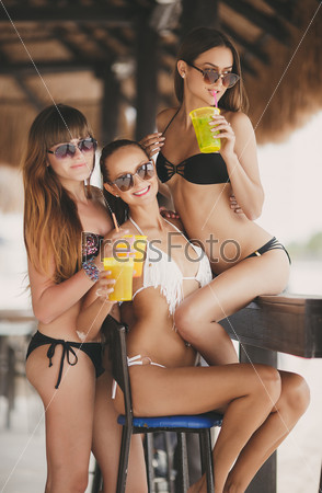 three beautiful sexy women in bikini in bar on Hawaii at beach bar. Beautiful girls enjoying alcoholic beverage cocktail outside. Smiling happy Caucasian women on Hawaiian beach.