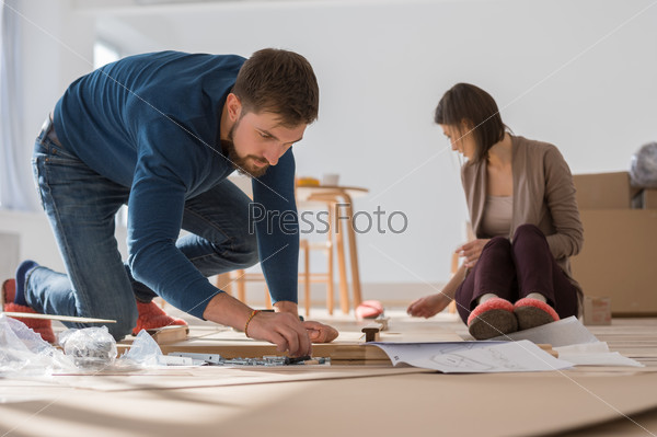 Happy young couple putting together self assembly furniture as they move into their new house.