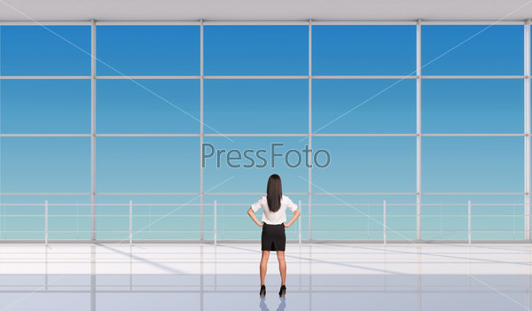 Young businesswoman with hands on waist in front of window, back view. Interior view