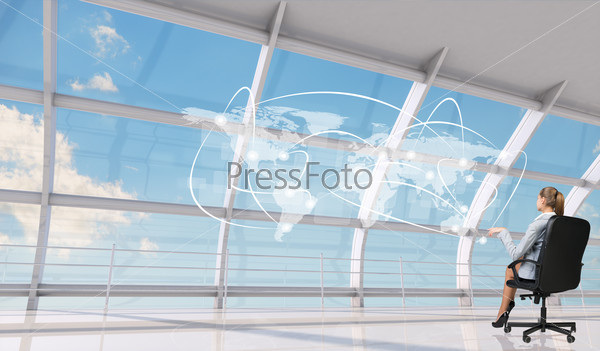 Rear view of businesswoman sitting in chair with crossed legs in front of window with virtual world map