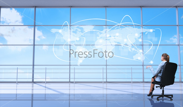 Rear view of businesswoman sitting in chair with crossed legs in front of window looking at virtual world map