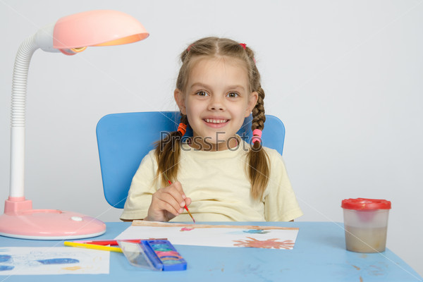 Six year old girl smiling happily, drawing the table