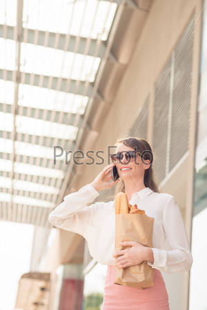 Modern business lady with a paper bag talking on the phone