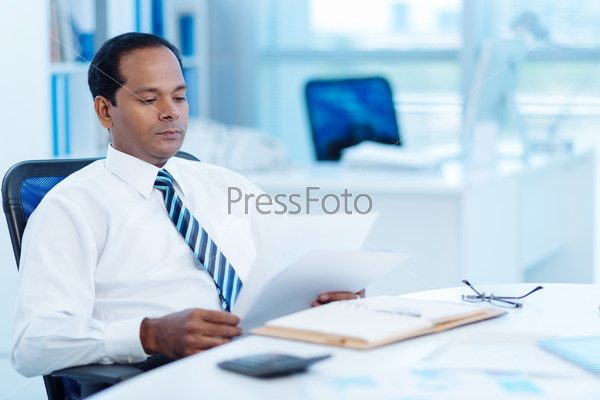 Indian entrepreneur reading business document at his workplace