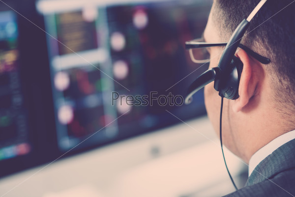 Close-up of broker in a headset analyzing data on the computer screen, selective focus