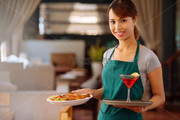 Young beautiful waitress carrying plate of chicken dish and a cocktail