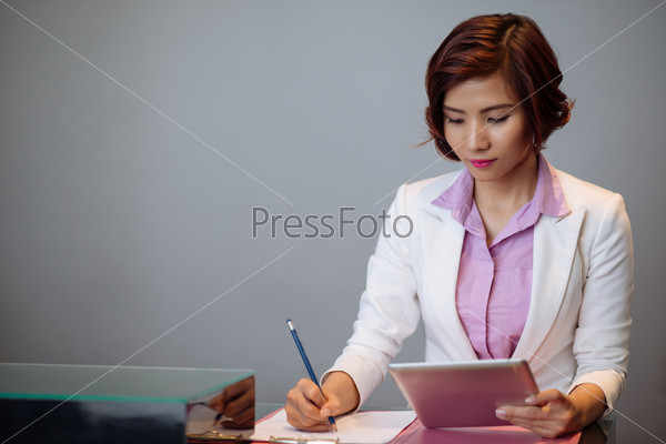 Beautiful business lady reading something on the digital tablet and making notes
