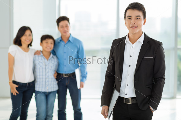 Portrait of confident young real estate broker and happy family in the background