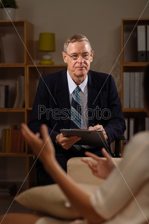 Senior psychiatrist listening to his patient and making notes