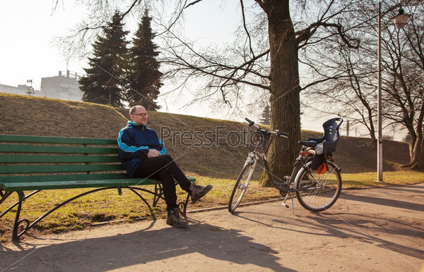 elderly man sitting on a bench near his bicycle in a city park