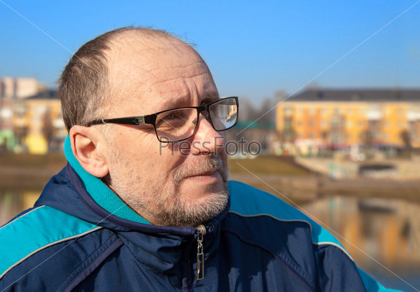 portrait of elderly man wearing glasses and a blue jacket in a city park