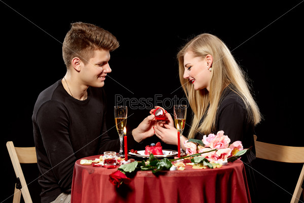 Man proposing marriage to a surprised woman on black background, stock photo