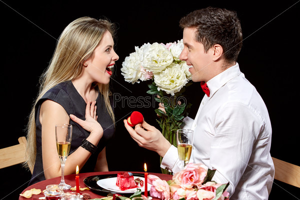 Man proposing marriage to a surprised woman on black background