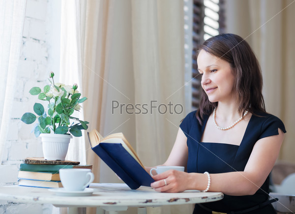 Young woman reading the book and drinking coffee in cafe