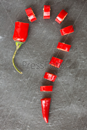 Cut red chilly pepper in shape of question mark, on gray background, top view