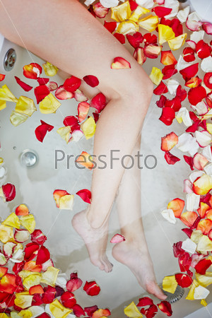 Bare female legs in bathtub with rose petals