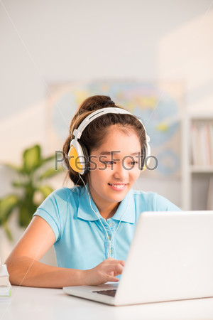 Asian preteen girl in headphones working on laptop