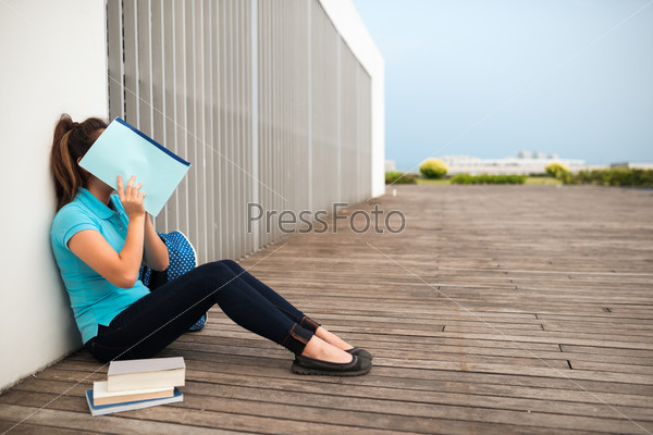 Shy college girl covering her face with a textbook