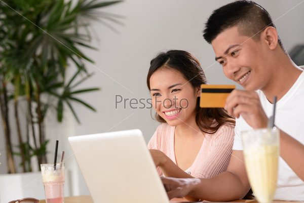 Cheerful Vietnamese couple using credit card to shop online