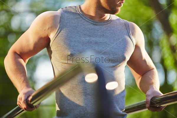 Active man in grey vest doing exercise for arms outdoor