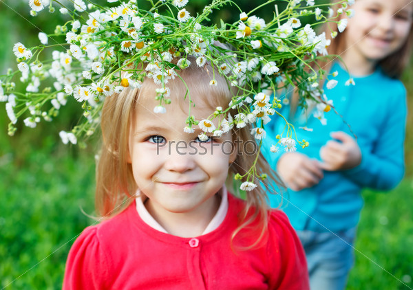 Portrait of two little sisters outdoors wearing wreath from white daisies in summer day. Focus on flowers