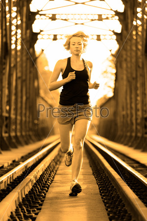 Athlete running on railway tracks bridge in morning sunrise training for marathon and fitness. Healthy sporty woman exercising in urban environment before going to work; Active urban lifestyle.