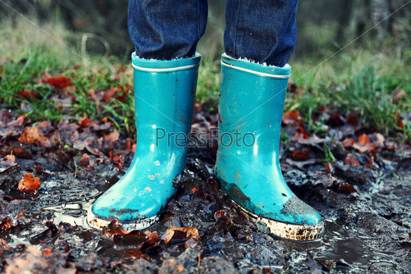 Fall / Autumn concept - Rain boots in mud puddle. Blue woman rain boots outdoors in action.