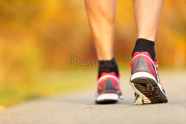 Running shoes closeup. Runner on road in fall autumn colors - closeup of male running walking shoes of jogger outdoors.