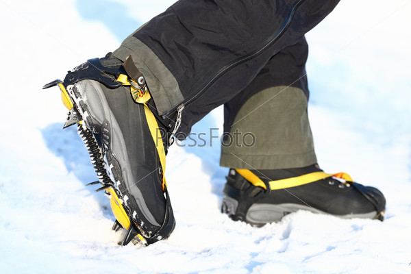 Crampons and shoes walking on ice and snow during outdoor winter trekking. Close up.