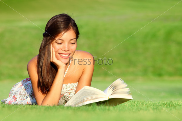 Reading. Woman reading book in park during spring / summer time. Happy smiling beautiful young university student studying lying down in grass. Mixed race Asian Chinese Caucasian female model outdoors