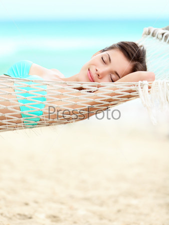 Vacation woman relaxing on beach in hammock on summer holidays resort. Beautiful happy multiracial Asian Chinese / Caucasian young woman.