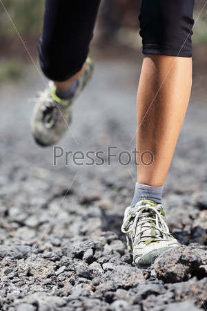 Trail runner woman running on mountain path with rocks. Running shoes and legs closeup of female fitness sport model during outdoor workout.