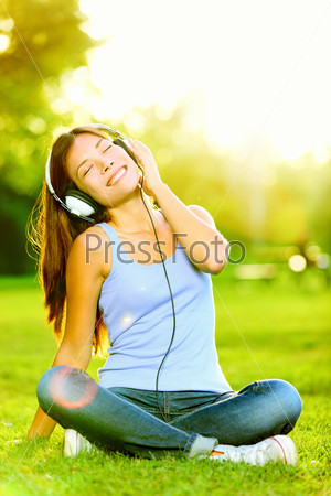 Woman listening to music. Female student girl outside in park\
listening to music on headphones while studying. Happy young\
university student of mixed Asian and Caucasian ethnicity.