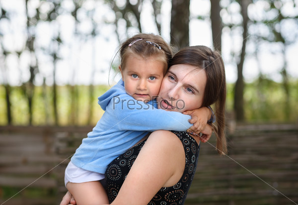 Mother and daughter embracing on blurred rural background. Selective on the faces of the models.