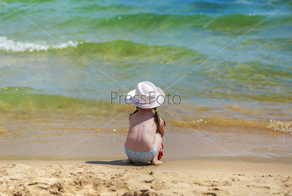 Child on the coast of tropical sea. Baby sits with his back to the camera, looking at the waves. Shallow depth of field. Selective focus on the model. Space for text.