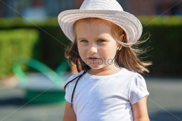A child with long hair in white hat and t-shirt. Clear sunny summer day. Shallow depth of field. Selective focus on the model\'s face.