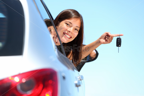 Woman driver holding car keys driving her new car. Beautiful multiracial young woman.