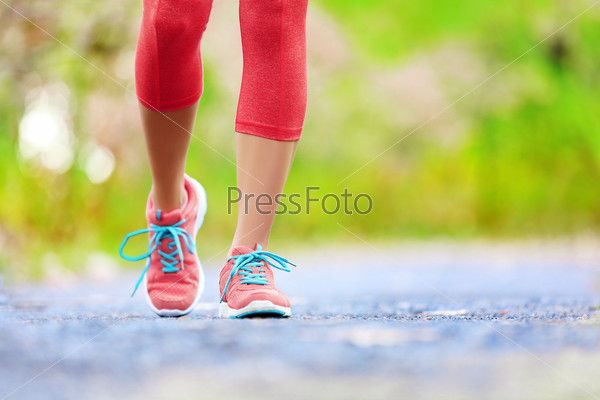 Jogging woman with athletic legs and running shoes. Female walking on trail in forest in healthy lifestyle concept with close up on running shoes. Female athlete jogger training outdoors.