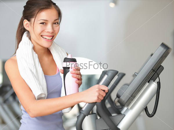 Gym woman fitness workout. Fitness girl exercising on moonwalker treadmill gym equipment. Young mixed-race Caucasian / Asian Chinese fitness model looking at camera smiling.