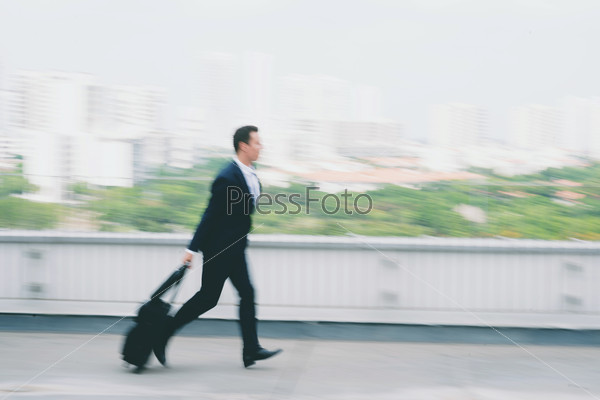 Businessman with a suitcase running late for flight, blurred motion
