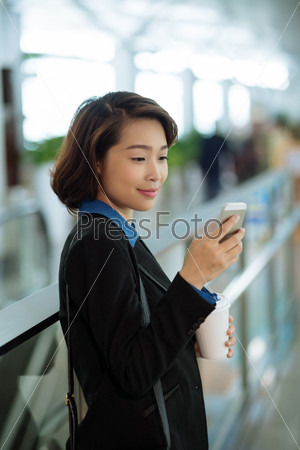 Smiling Asian lady with a cup of coffee reading message on her phone