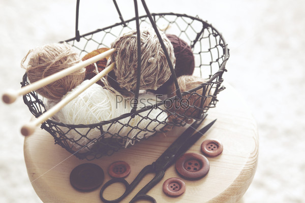 Vintage knitting needles, scissors and yarn inside old wire basket on wooden stool, still life photo with soft focus